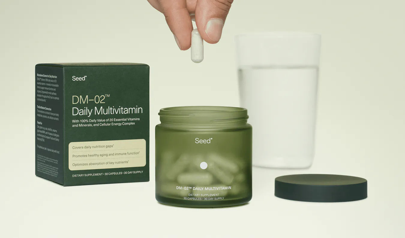 Seed Daily Multivitamin jar with packaging and a hand holding a supplement capsule.