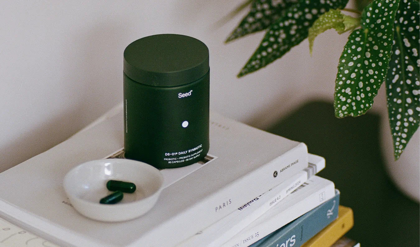 Dark green supplement container with pills on a stack of books next to a plant