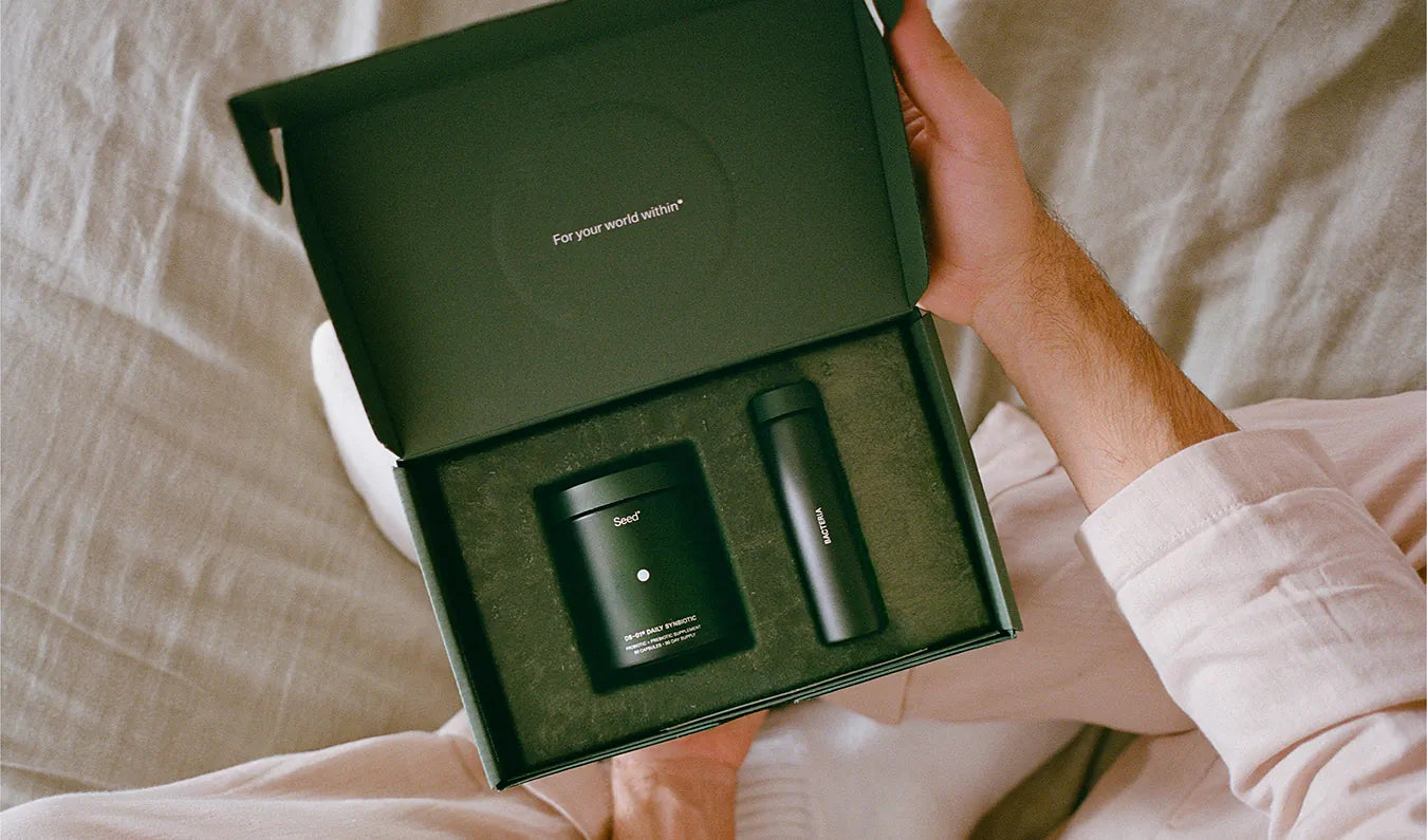 Person holding a green box with two black items inside, likely a travel mug and container.